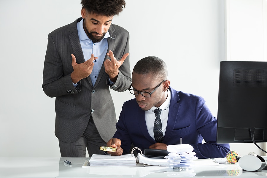 Picture of a man watching someone review the fine print of a document. The watcher has his fingers crossed.